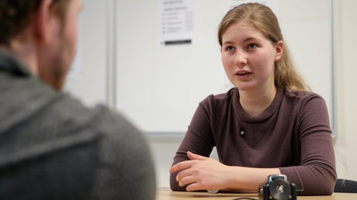 Девушка разговаривает с преподавателем за столом в учебном классе.